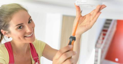Jonge vrouw hangt rookmelder aan plafond